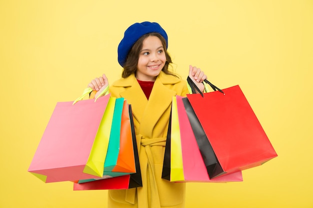 Ottieni uno sconto per lo shopping per il compleanno o le vacanze Fashionista adora lo shopping Ossessionato dallo shopping Ragazza carino bambino tenere borse della spesa su sfondo giallo Saldi di mezza stagione Acquista con carta sconto