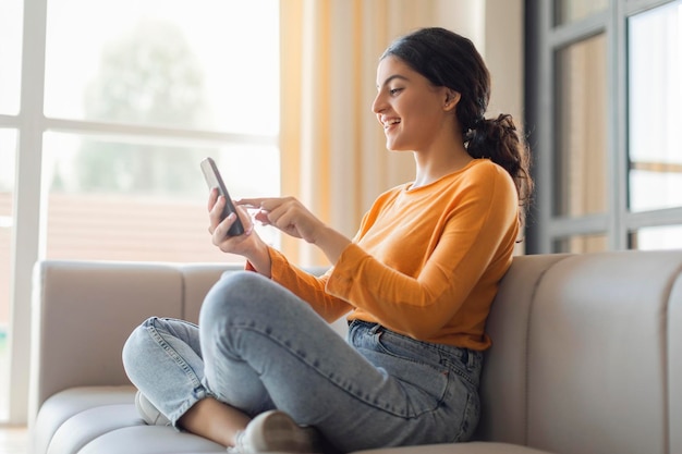 Ottima app allegra donna indiana che naviga l'applicazione sullo smartphone a casa