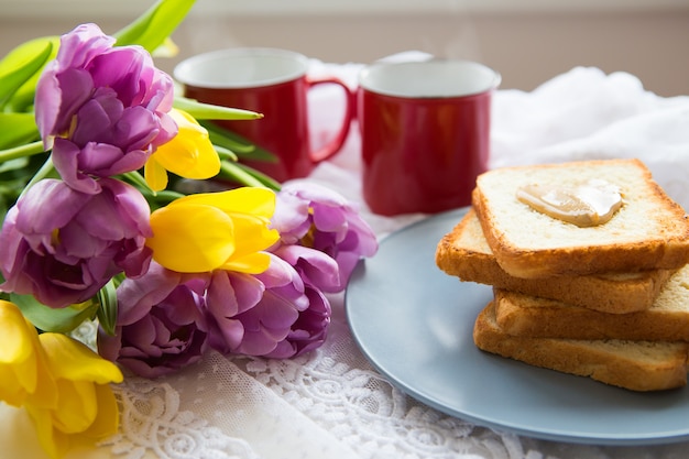 Ottima colazione Due tazze di caffè, toast con burro di arachidi e un bellissimo bouquet luminoso di tulipani.