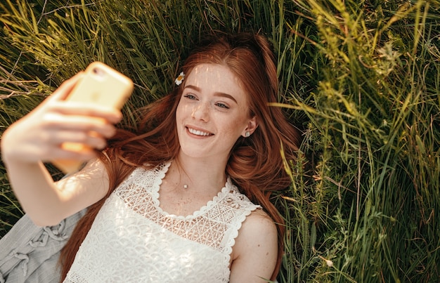 Ottimista giovane femmina con i capelli di zenzero sorridente e prendendo selfie