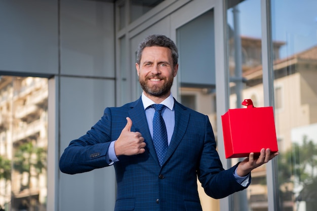 Ottimo regalo. Uomo con confezione regalo e sorridente in piedi contro la città.