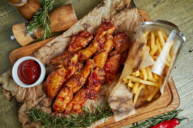 Ottimo spuntino alla birra - ali di bufalo speziate al forno. Ali del BBQ con il contorno delle patate fritte su un vassoio di legno. Vista dall'alto, cibo piatto disteso. Cibo da pub