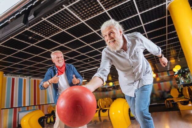 Ottimo tiro. Allegro uomo positivo che sorride mentre lancia la palla da bowling