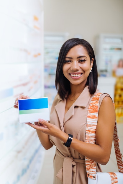 Pacchetto colorato. Bruna carina che mantiene il sorriso sul viso mentre mostra le vitamine preferite