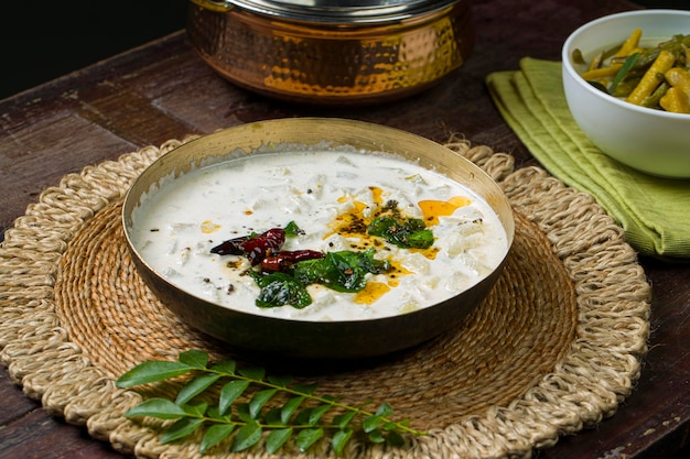 Pachadi o Raitha e olanKerala festa contorni piatti vegetariani disposti in un recipiente di ottone e ciotola bianca che è posto su sfondo di legno