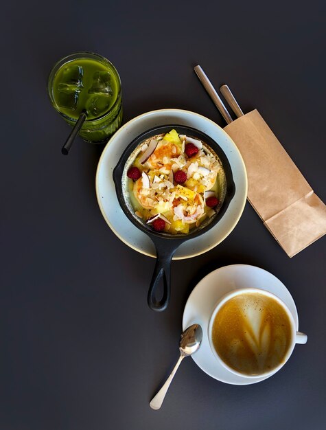 Padella con cheesecake o pancake e frutti di bosco, tazza di caffè e Matcha sul tavolo scuro, vista dall'alto.