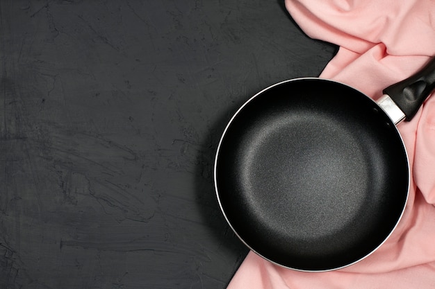 Padella nera vuota con l'asciugamano di cucina rosa sulla tavola nera.