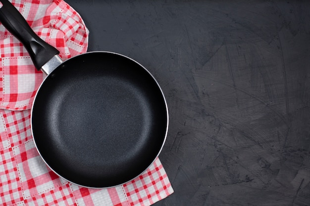 Padella nera vuota con l'asciugamano di cucina sulla tavola nera.