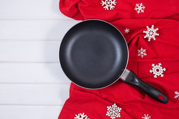 Padella o padella con fiocchi di neve e tovaglia rossa sulla tavola di legno.