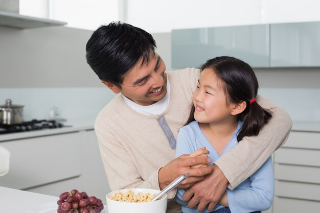 Padre allegro con la figlia che mangia i cereali in cucina