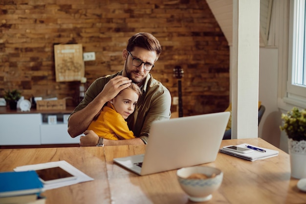 Padre amorevole che legge un'e-mail sul laptop mentre era con sua figlia a casa