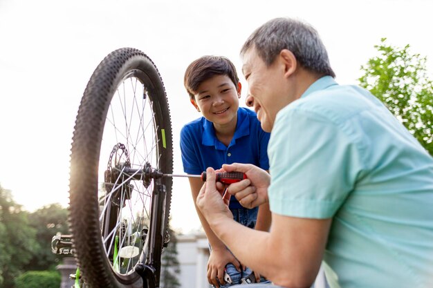 padre asiatico che aiuta il figlio a riparare la bicicletta con gli attrezzi ragazzo coreano che guarda il padre riparare una bicicletta rotta