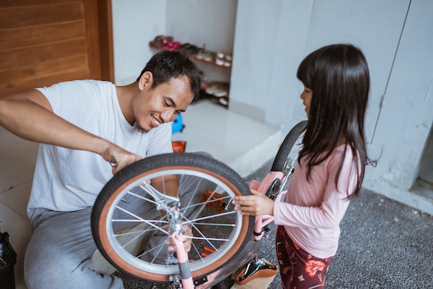 Padre asiatico che usa una chiave inglese per riparare la bicicletta con la figlia