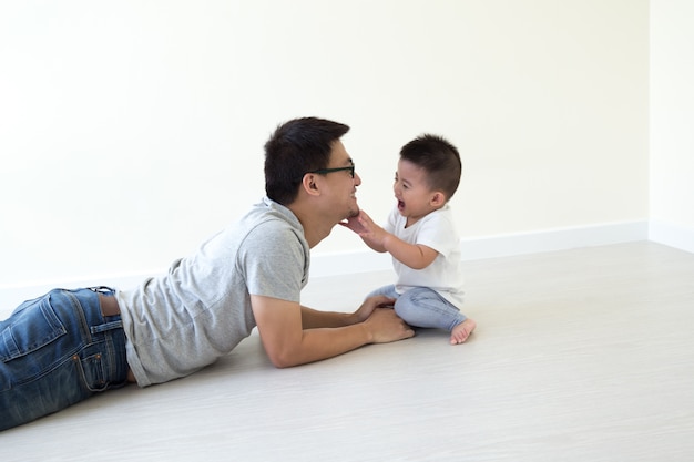 Padre asiatico e figlio che giocano e che sorridono sul pavimento nella stanza