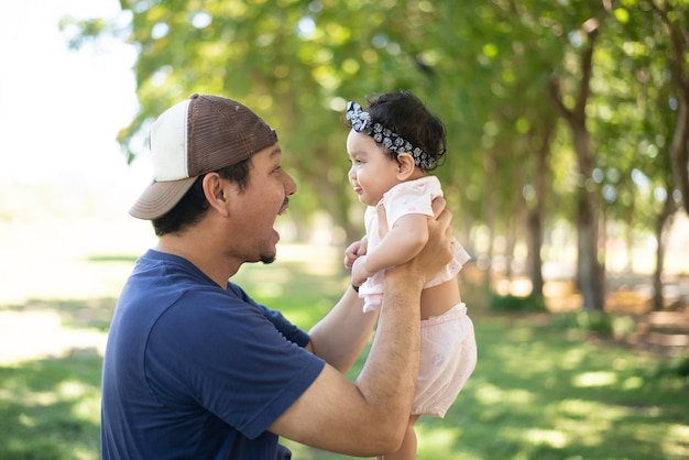 padre asiatico felice che tiene in mano una bambina carina su sfondo sfocato di giardino verde