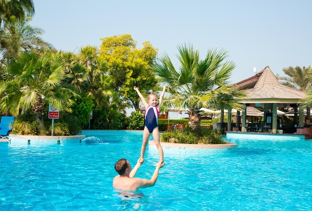 Padre attivo che insegna a sua figlia a nuotare in piscina in un resort tropicale Vacanze estive e concetto di sport