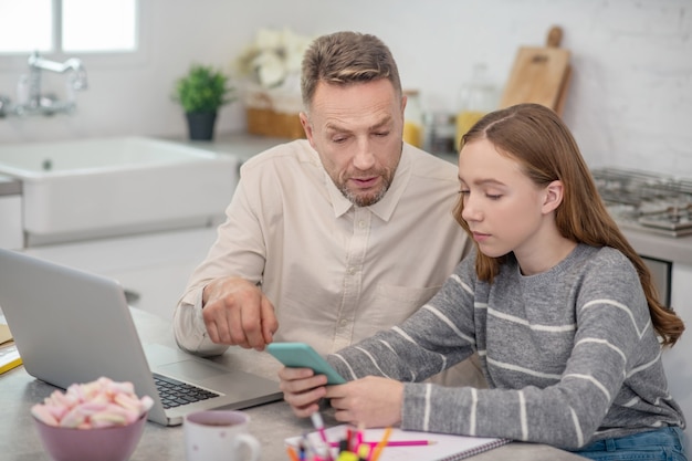 Padre barbuto che indica qualcosa sullo smartphone delle figlie