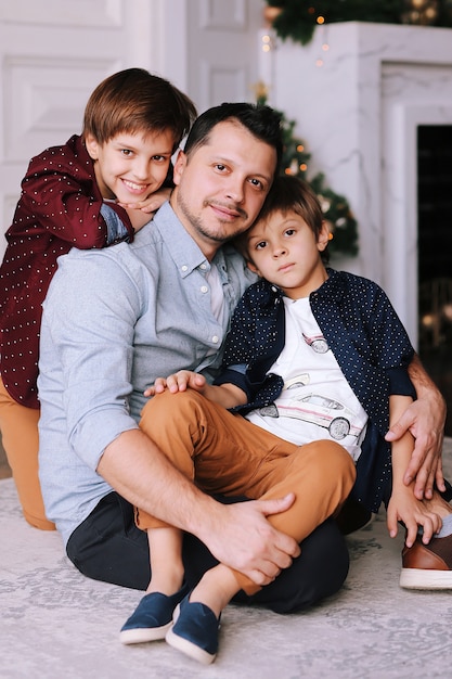 Padre bello che gioca e che sorride con i suoi figli divertenti accanto all'albero di Natale a casa