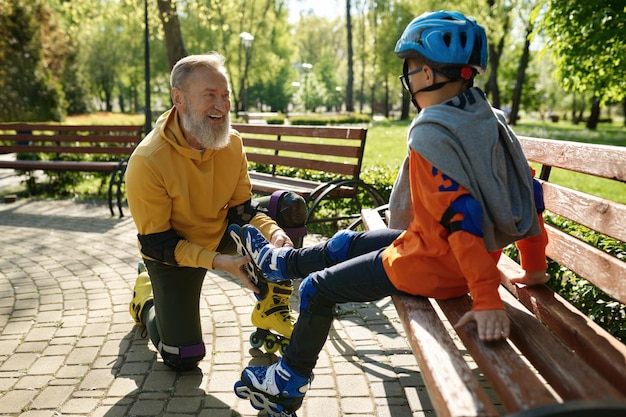 Padre che aiuta il figlio a indossare i pattini a rotelle. Riposo attivo della famiglia felice e tempo libero per il tempo libero nel parco urbano durante il fine settimana