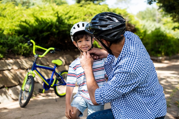Padre che assiste il figlio nell'uso del casco da bicicletta nel parco