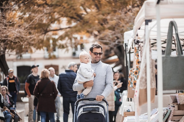 Padre che cammina portando il suo bambino e spingendo il passeggino in una folla di persone