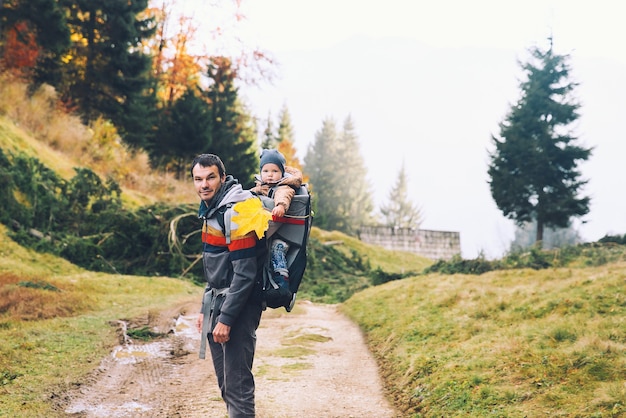 Padre che fa un'escursione con il bambino nello zaino del marsupio sulla natura nella foresta autunnale Famiglia in montagna