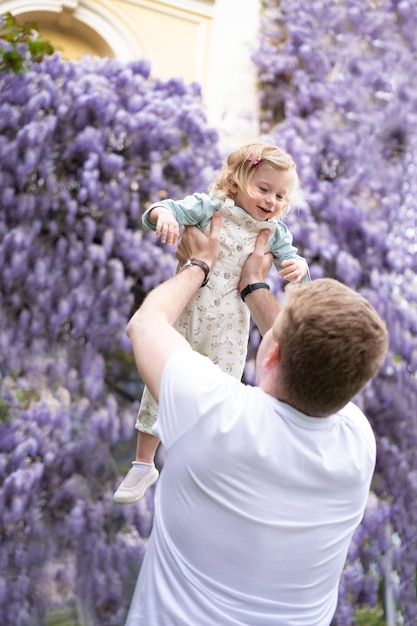 Padre che gioca divertendosi all'aperto con la bambina su sfondo di glucinum flowerpurplevery peri