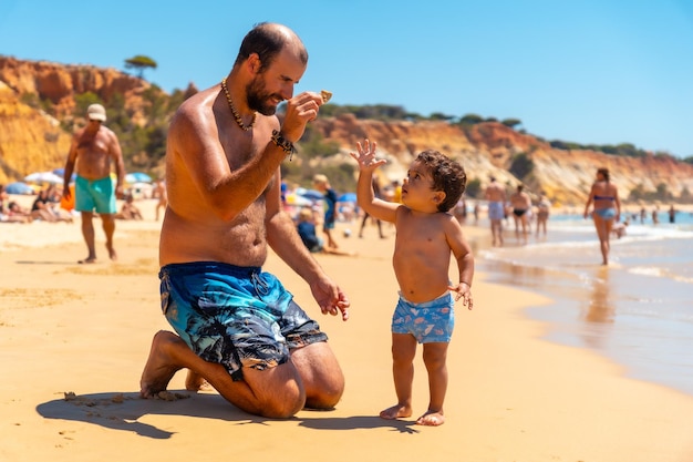 Padre che gioca nella sabbia Praia do Barranco das Belharucas spiaggia Albufeira Algarve Portogallo