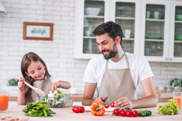 Padre che guarda sua figlia che prepara l'insalata sulla cucina