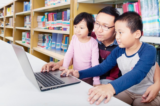 Padre che guida i bambini su come utilizzare il laptop in biblioteca