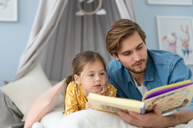 Padre che legge un libro a sua figlia sdraiato sul pavimento in camera da letto.