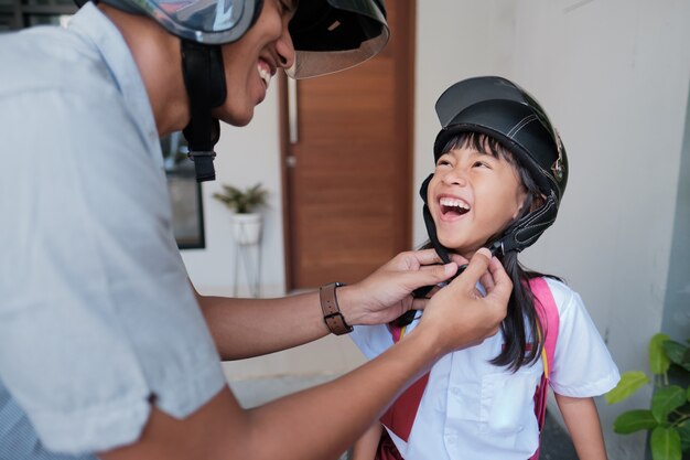 Padre che porta sua figlia a scuola in moto al mattino. allacciare il casco