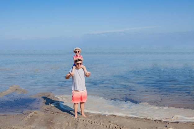 Padre che tiene il figlio sulle spalle in spiaggia.