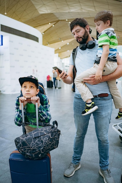 Padre che tiene un ragazzo caucasico carino in aeroportofamiglia in attesa di un volo in ritardo Viaggiare con i bambini