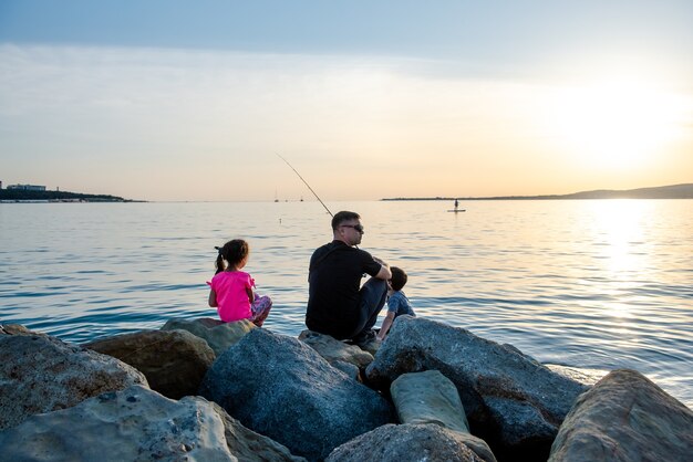 Padre con bambini durante una battuta di pesca in mare I bambini pescano da una scogliera nel mare