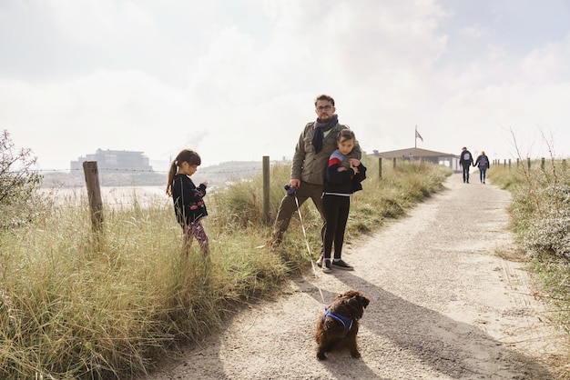 Padre con due figlie e un cane sull'erba contro il cielo