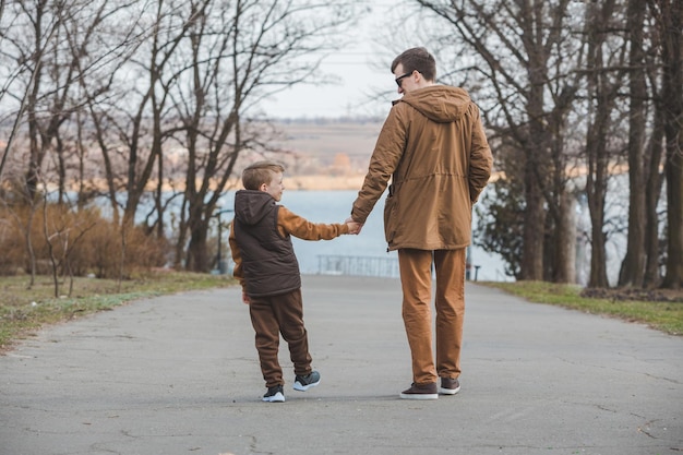 Padre con figlio che cammina dal parco tenendosi per mano vista posteriore