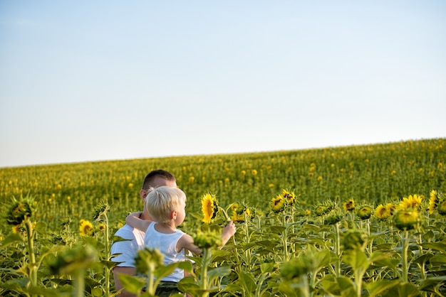 Padre con il figlio piccolo tra le braccia in piedi su un campo di girasoli