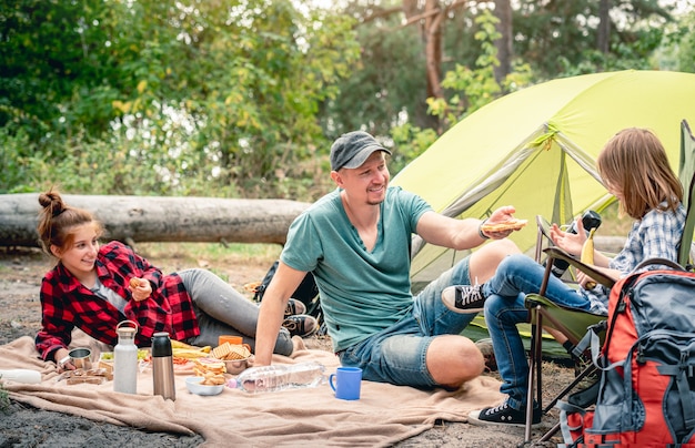 Padre con le figlie sul picnic vicino alla tenda nella foresta