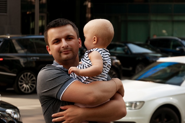 Padre con un bambino di un anno tra le braccia. Cammina in un ambiente urbano.