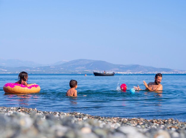 Padre di famiglia, figlia e figlio giocano e versano acqua sulla spiaggia di un'isola greca in una giornata estiva