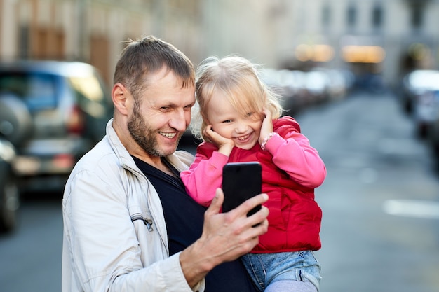 Padre e bambina stanno guardando video sul telefono all'aperto