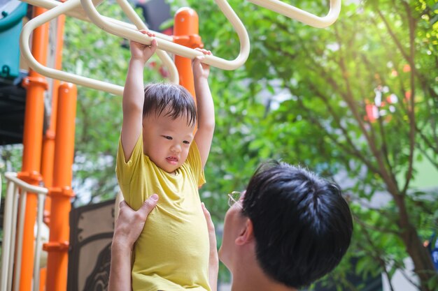 Padre e Carino piccolo asiatico 2 - 3 anni bambino bambino bambino bambino divertirsi esercitando all'aperto e papà aiuta a recuperare il ritardo sulle attrezzature di Monkey Bar al parco giochi