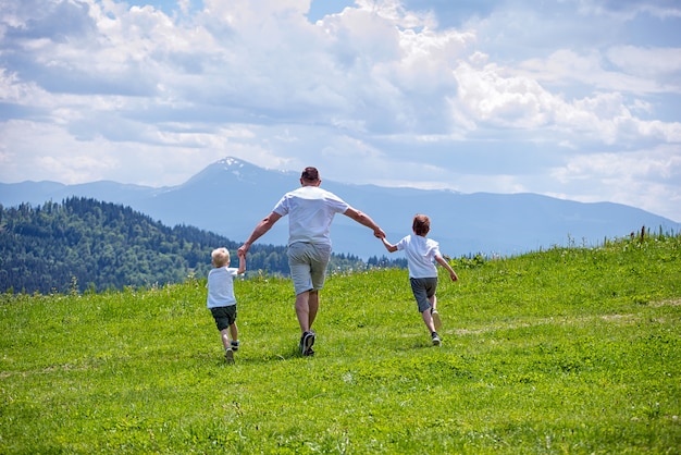 Padre e due giovani figli che corrono sul campo verde tenendosi per mano
