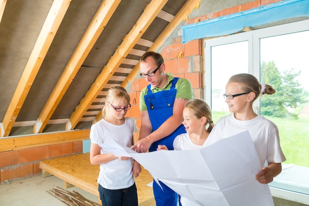 Padre e figli o figlie e amici che esaminano un piano di costruzione in un cantiere