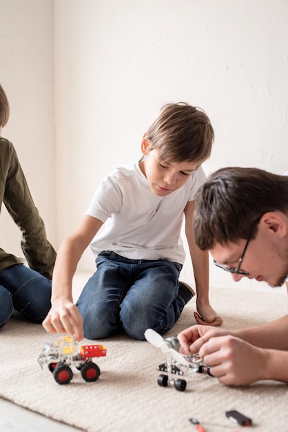 Padre e figli trascorrono del tempo insieme, divertendosi a costruire auto robot a casa seduti sul tappeto