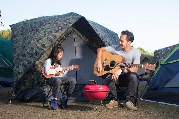 Padre e figlia al campeggio giocando ukulele e chitarra