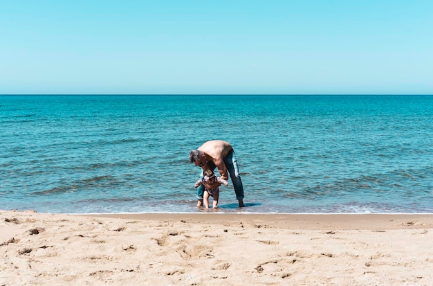 Padre e figlia che giocano sulla spiaggia con acqua di mare in una giornata di sole durante le vacanze estive Famiglia persone che si divertono insieme all'aperto Viaggi e felicità lifestyle Concetto di genitori single