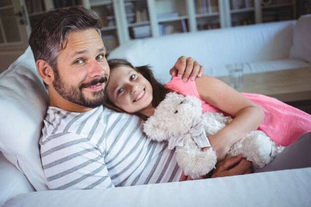 Padre e figlia sorridenti che si siedono sul sofà con un orsacchiotto