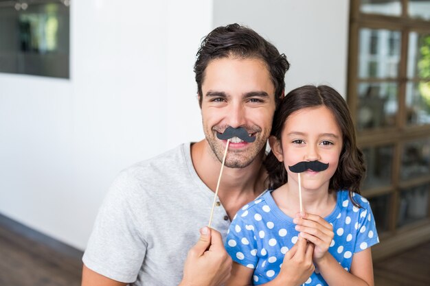 Padre e figlia sorridenti con i baffi artificiali